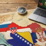 Stara geografska mapa Balkana sa istaknutim zastavama Slovenije, Hrvatske, Bosne i Hercegovine i Srbije. Na drvenom stolu pored mape nalaze se lupa, kompas i otvoren laptop sa natpisom "Online Casino", što simbolizuje istraživanje i navigaciju kroz tržište onlajn kazina u regionu.